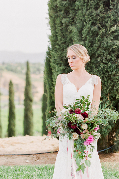 Temecula outdoor wedding at callaway winery bride form fitting lace gown with crystal beading and lace detail with open back design and beaded straps holding pink and green floral bridal bouquet