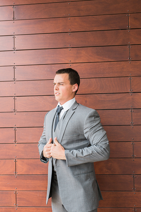 Temecula outdoor wedding at callaway winery groom grey notch lapel suit with matching vest and white dress shirt with long black skinny tie and white and pink floral boutonniere holding jacket getting ready before ceremony