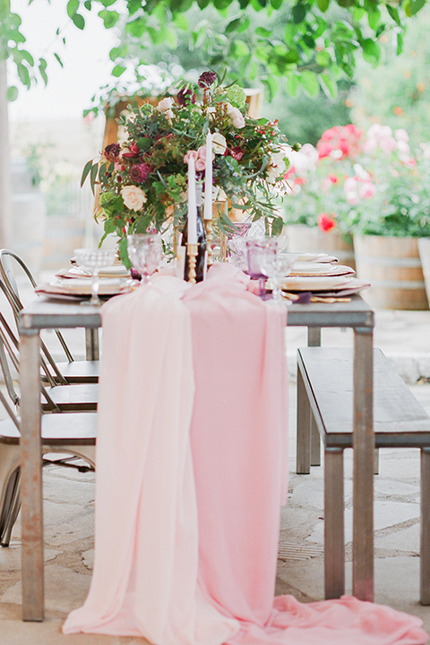 Temecula outdoor wedding at callaway winery table set up light brown wood table with blush pink table runner and white and green flower centerpiece decor with white and gold place settings with blush pink napkins and white and brown vintage chairs