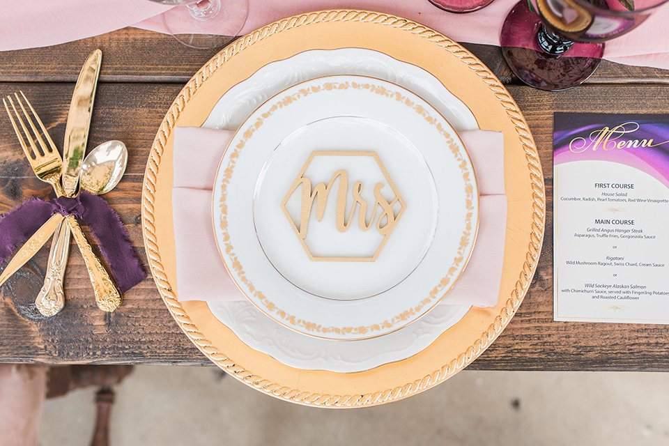 Temecula outdoor wedding at callaway winery table set up light brown wood table with blush pink table runner and white and green flower centerpiece decor with white and gold place settings with blush pink napkins and white and brown vintage chairs