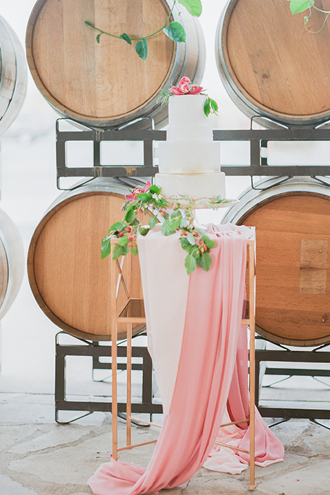 Temecula outdoor wedding at callaway winery wedding cake three tier white cake with pink flower decor on top and greenery floral decor on side with blush pink table linen decor and wine barrels in background wedding photo idea for cake