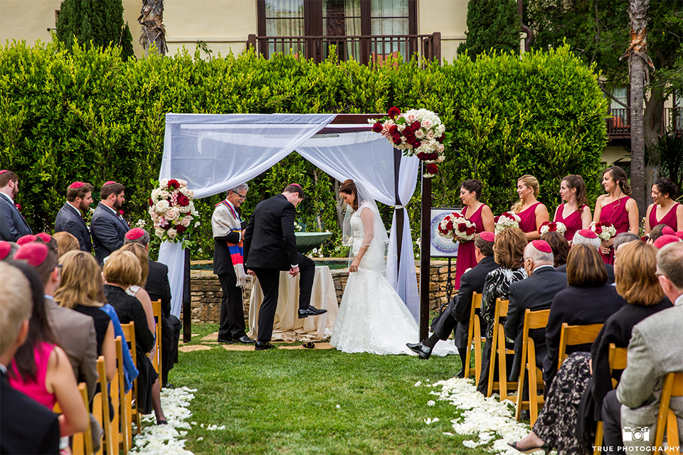 San diego beach wedding at estancia la jolla bride form fitting strapless gown with sweetheart neckline and lace design with long veil and groom black shawl lapel tuxedo with matching vest and white dress shirt with black bow tie and white pocket square with white floral boutonniere ceremony