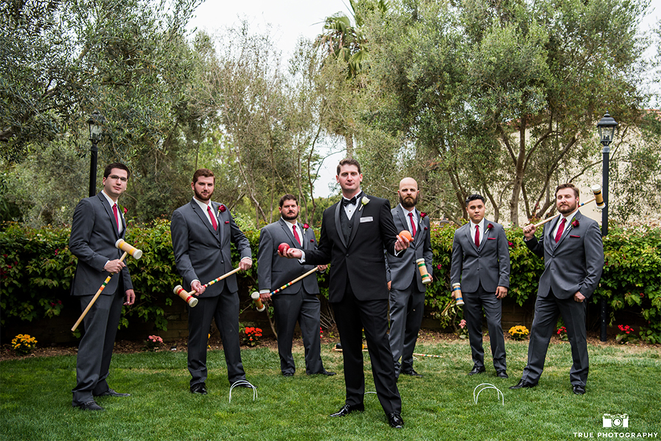 San diego beach wedding at estancia la jolla groom black shawl lapel tuxedo with black bow tie and white dress shirt with white pocket square and white floral boutonniere with groomsmen charcoal grey suits with long red ties