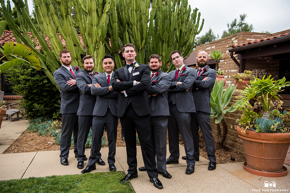 San diego beach wedding at estancia la jolla groom black shawl lapel tuxedo with black bow tie and white dress shirt with white pocket square and white floral boutonniere with groomsmen charcoal grey suits with long red ties