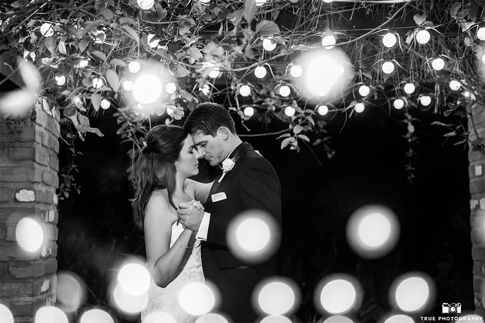 San diego beach wedding at estancia la jolla bride form fitting strapless gown with sweetheart neckline and lace design with long veil and groom black shawl lapel tuxedo with matching vest and white dress shirt with black bow tie and white pocket square with white floral boutonniere dancing black and white photo