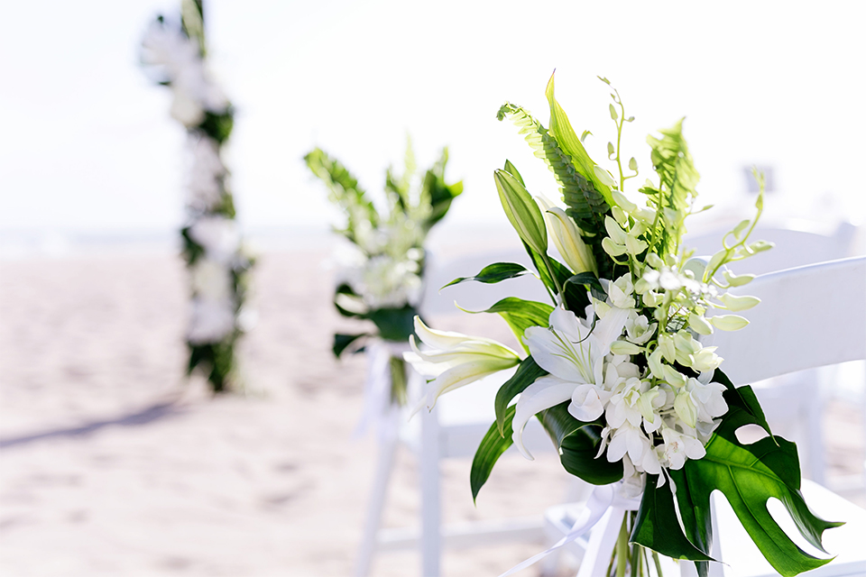 Huntington beach wedding at the hilton waterfront resort table set up white table linen with white and green floral centerpiece decor with white table numbers written on green leaves and glass candle decor with dark chairs
