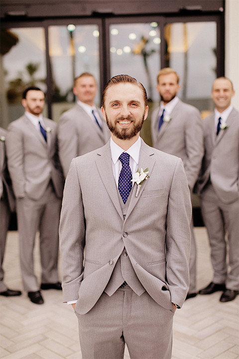 Huntington beach wedding at the hilton waterfront resort groom and groomsmen heather grey notch lapel suits with matching vests and white dress shirt with long navy blue patterned tie and white floral boutonnieres standing with hands in pockets