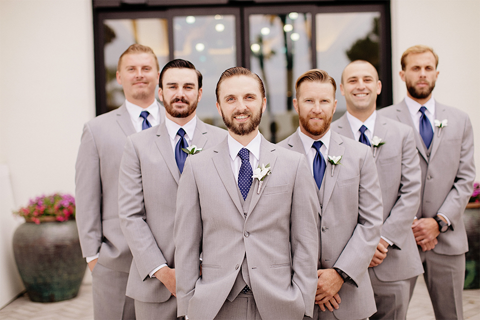 Huntington beach wedding at the hilton waterfront resort groom and groomsmen heather grey notch lapel suits with matching vests and white dress shirt with long navy blue patterned tie and white floral boutonnieres standing with hands crossed