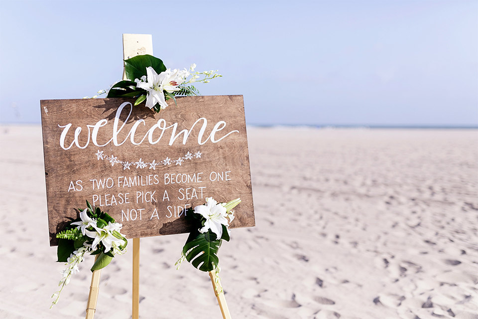 Huntington beach wedding at the hilton waterfront resort wedding ceremony altar with brown wood and white and green flower decor on sand wedding photo idea for ceremony altar and welcome sign rustic decor light brown wood sign with white calligraphy writing and white and green flower decor