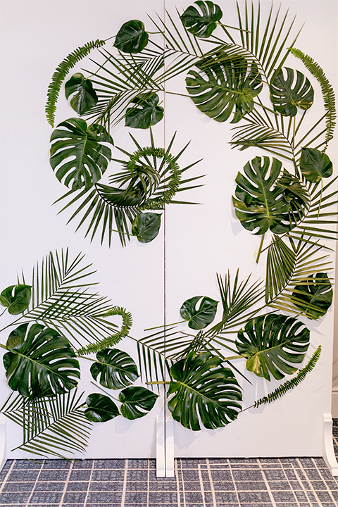 Huntington beach wedding at the hilton waterfront resort table set up white table linen with white and green floral centerpiece decor with white table numbers written on green leaves and glass candle decor with dark chairs with green leaves on wall for decor