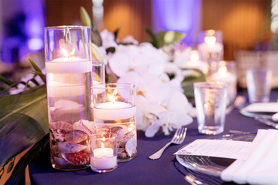 Huntington beach wedding at the hilton waterfront resort table set up white table linen with white and green floral centerpiece decor with white table numbers written on green leaves and glass candle decor with dark chairs