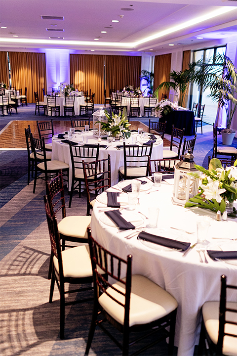 Huntington beach wedding at the hilton waterfront resort table set up white table linen with white and green floral centerpiece decor with white table numbers written on green leaves and glass candle decor with dark chairs