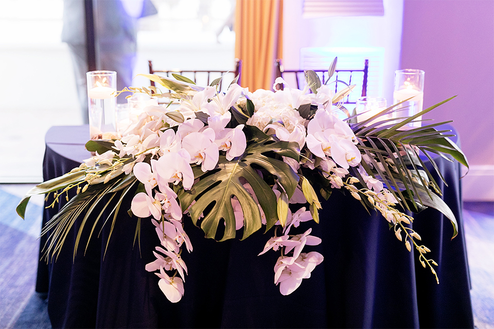 Huntington beach wedding at the hilton waterfront resort table set up white table linen with white and green floral centerpiece decor with white table numbers written on green leaves and glass candle decor with dark chairs