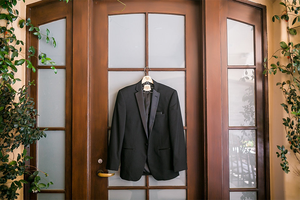 San juan capistrano outdoor wedding at plaza de magdelena groom getting ready black notch lapel tuxedo hanging on hanger on the door wedding photo idea for grooms attire