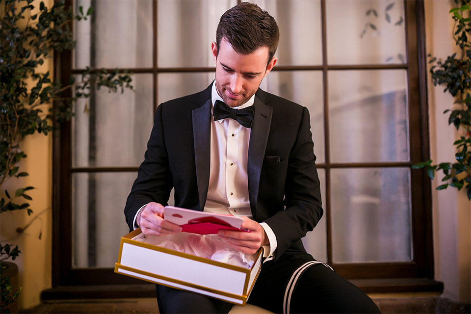 San juan capistrano outdoor wedding at plaza de magdelena groom black notch lapel tuxedo with white dress shrirt and black bow tie with white floral boutonniere opening present from bride