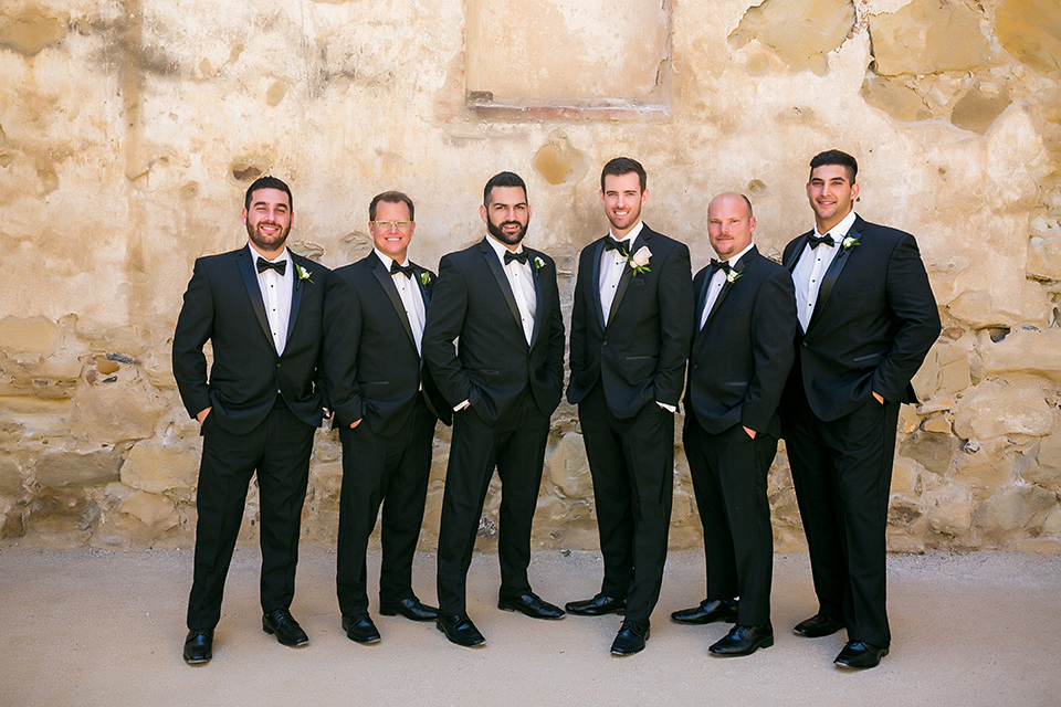 San juan capistrano outdoor wedding at plaza de magdelena groom black notch lapel tuxedo with white dress shrirt and black bow tie with white floral boutonniere with groomsmen black notch lapel tuxedos with black bow ties and white floral boutonnieres