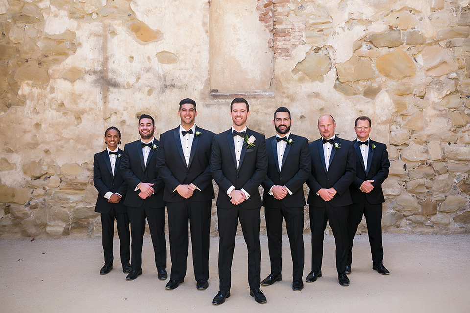 San juan capistrano outdoor wedding at plaza de magdelena groom black notch lapel tuxedo with white dress shrirt and black bow tie with white floral boutonniere with groomsmen black notch lapel tuxedos with black bow ties and white floral boutonnieres