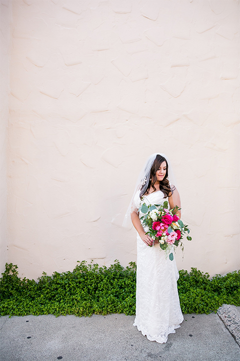 San juan capistrano outdoor wedding at plaza de magdelena bride form fitting gown with lace detail on bodice and thin straps with crystal belt holding white and pink floral bridal bouquet