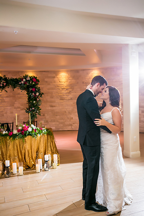 San juan capistrano outdoor wedding at plaza de magdelena bride form fitting gown with lace detail on bodice and thin straps with crystal belt and groom black notch lapel tuxedo with white dress shirt and black bow tie and white floral boutonniere first dance