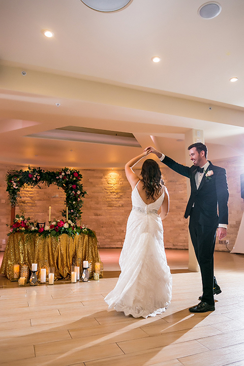 San juan capistrano outdoor wedding at plaza de magdelena bride form fitting gown with lace detail on bodice and thin straps with crystal belt and groom black notch lapel tuxedo with white dress shirt and black bow tie and white floral boutonniere first dance