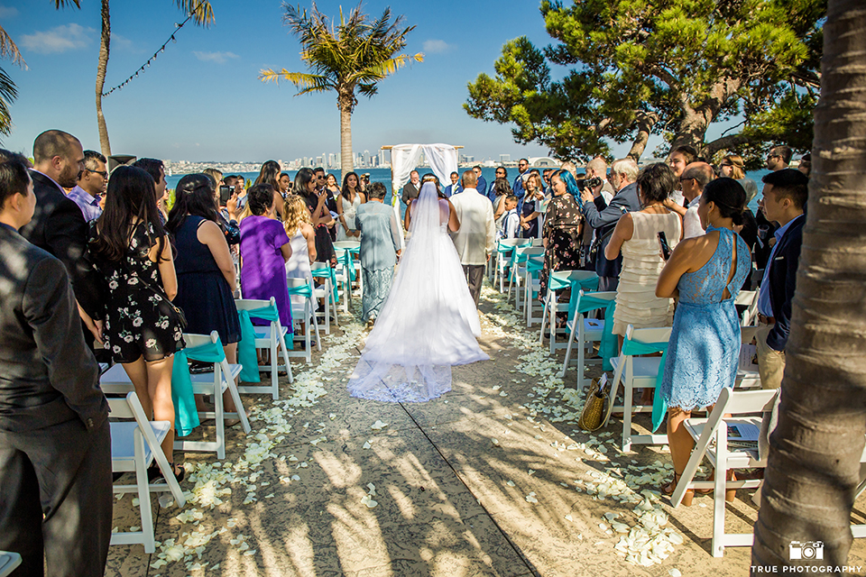 San diego outdoor wedding at bali hai bride ball gown with thin lace straps and a sweetheart neckline with lace and beading detail on bodice with long veil walking down aisle with parents