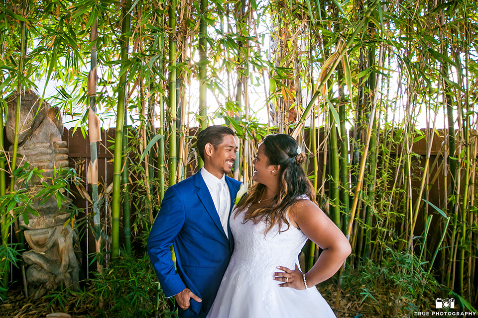 San diego outdoor wedding at bali hai bride ball gown with thin lace straps and a sweetheart neckline with lace and beading detail on bodice with long veil with groom cobalt blue notch lapel suit with white dress shirt and white vest with long white striped tie and pocket square with white floral boutonniere hugging and smiling