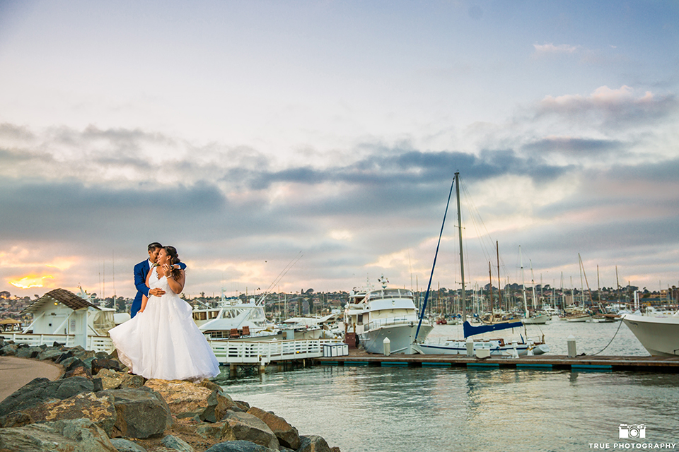 San diego outdoor wedding at bali hai bride ball gown with thin lace straps and a sweetheart neckline with lace and beading detail on bodice with long veil with groom cobalt blue notch lapel suit with white dress shirt and white vest with long white striped tie and pocket square with white floral boutonniere hugging far away