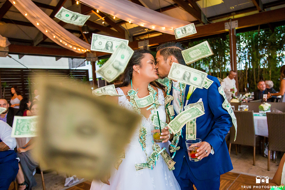 San diego outdoor wedding at bali hai bride ball gown with thin lace straps and a sweetheart neckline with lace and beading detail on bodice with long veil with groom cobalt blue notch lapel suit with white dress shirt and white vest with long white striped tie and pocket square with white floral boutonniere kissing during money dance at reception