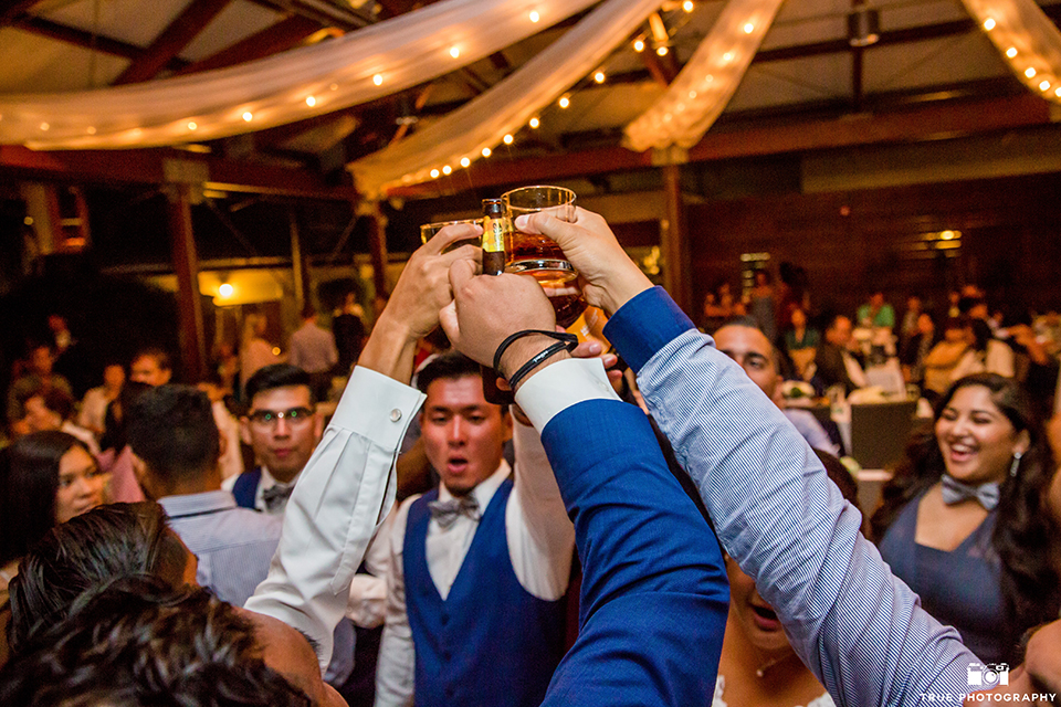 San diego outdoor wedding at bali hai bride ball gown with thin lace straps and a sweetheart neckline with lace and beading detail on bodice with long veil with groom cobalt blue notch lapel suit with white dress shirt and white vest with long white striped tie and pocket square with white floral boutonniere guys holding drinks in the air at reception