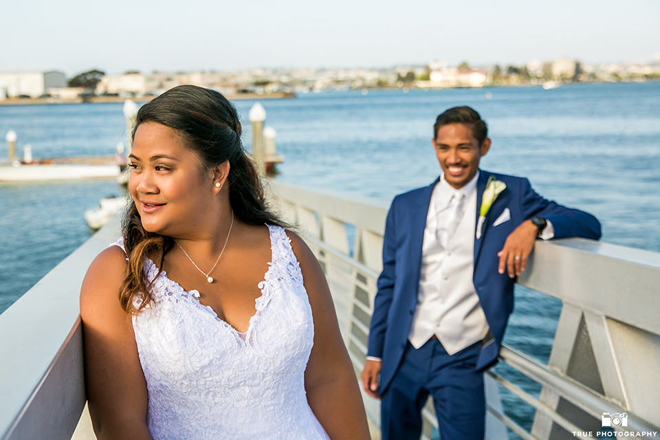 San diego outdoor wedding at bali hai bride ball gown with thin lace straps and a sweetheart neckline with lace and beading detail on bodice with long veil with groom cobalt blue notch lapel suit with white dress shirt and white vest with long white striped tie and pocket square with white floral boutonniere standing and smiling