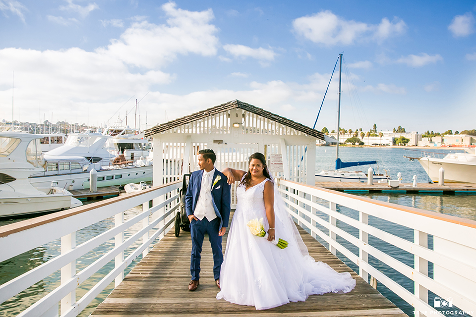 San diego outdoor wedding at bali hai bride ball gown with thin lace straps and a sweetheart neckline with lace and beading detail on bodice with long veil with groom cobalt blue notch lapel suit with white dress shirt and white vest with long white striped tie and pocket square with white floral boutonniere standing and bride holding white floral bridal bouquet