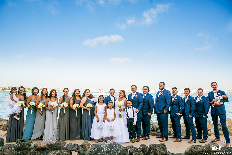 San diego outdoor wedding at bali hai bride ball gown with thin lace straps and a sweetheart neckline with lace and beading detail on bodice with long veil with groom cobalt blue notch lapel suit with white dress shirt and white vest with long white striped tie and pocket square with white floral boutonniere with wedding party bridesmaids mix and matched dresses and groomsmen 