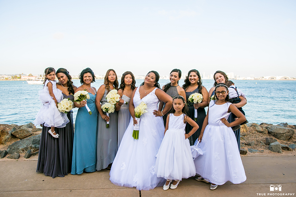 San diego outdoor wedding at bali hai bride ball gown with thin lace straps and a sweetheart neckline with lace and beading detail on bodice with long veil holding white floral bridal bouquet with bridesmaids long mix and matched dresses