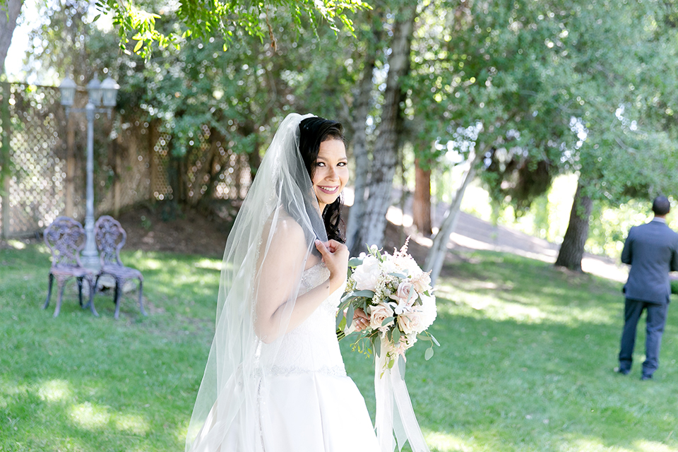 Temecula outdoor wedding at lake oak meadows bride a line strapless gown with lace and detail beading on bodice and long veil holding white and green floral bridal bouquet first look behind groom wedding photo idea for first look