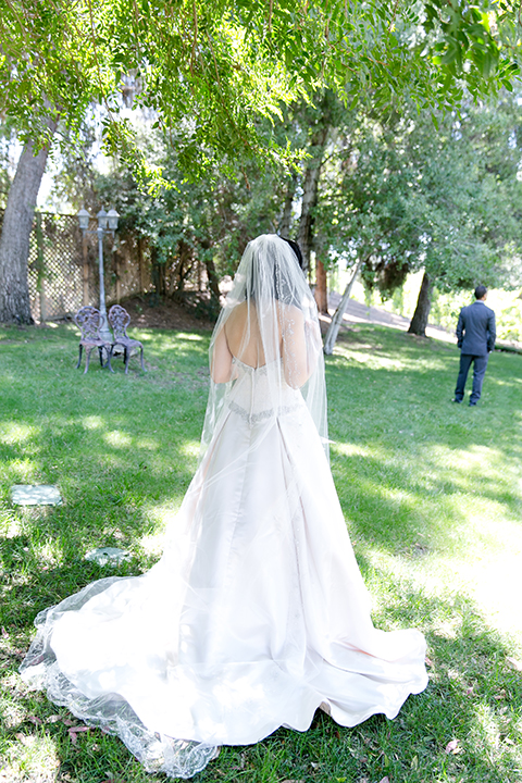 Temecula outdoor wedding at lake oak meadows bride a line strapless gown with lace and detail beading on bodice and long veil with groom grey notch lapel suit with light grey vest and white dress shirt with light grey matching bow tie and white floral boutonniere first look bride behind groom