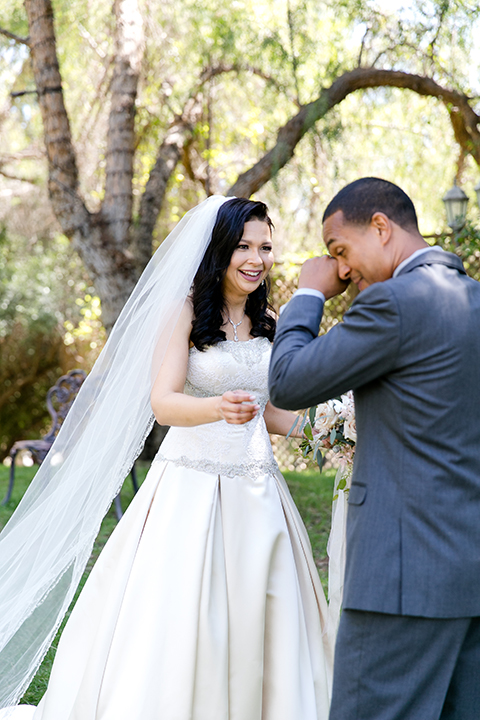 Temecula outdoor wedding at lake oak meadows bride a line strapless gown with lace and detail beading on bodice and long veil with groom grey notch lapel suit with light grey vest and white dress shirt with light grey matching bow tie adn white floral boutonniere first look groom crying