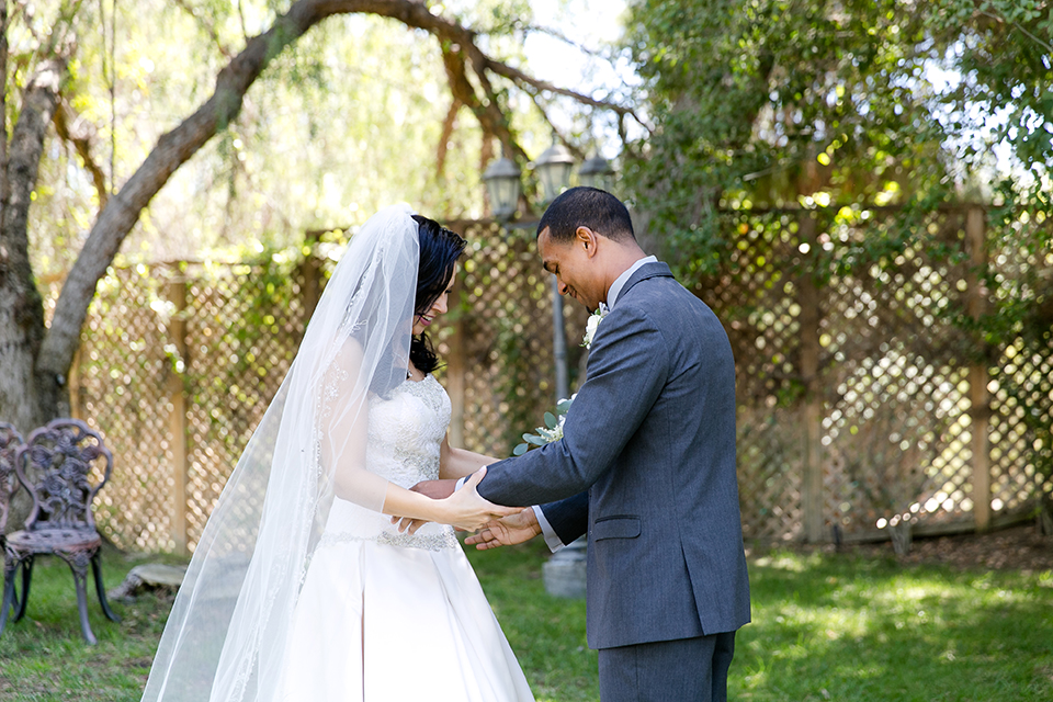 Temecula outdoor wedding at lake oak meadows bride a line strapless gown with lace and detail beading on bodice and long veil with groom grey notch lapel suit with light grey vest and white dress shirt with light grey matching bow tie adn white floral boutonniere first look bride and groom holding hands