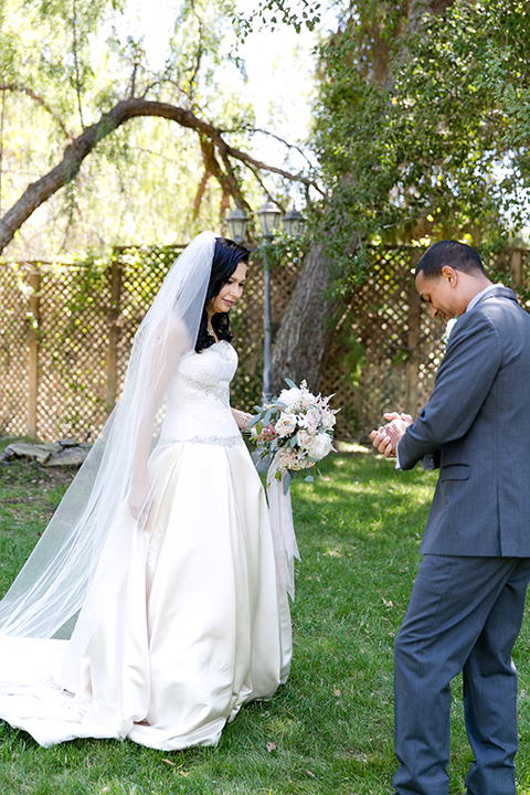 Temecula outdoor wedding at lake oak meadows bride a line strapless gown with lace and detail beading on bodice and long veil with groom grey notch lapel suit with light grey vest and white dress shirt with light grey matching bow tie adn white floral boutonniere first look bride holding white and green floral bridal bouquet