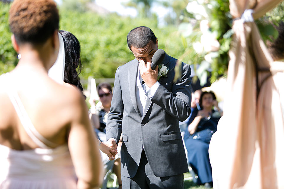 Temecula outdoor wedding at lake oak meadows bride a line strapless gown with lace and detail beading on bodice and long veil with groom grey notch lapel suit with light grey vest and white dress shirt with light grey matching bow tie adn white floral boutonniere groom crying during ceremony