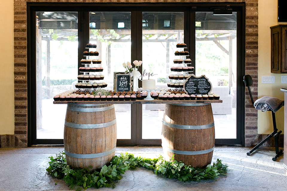 Temecula outdoor wedding at lake oak meadows dessert table assortment of sweets on two wine barrels and table with black and white sign for decor and white one tier wedding cake with gold love calligraphy cake topper with greenery floral decor