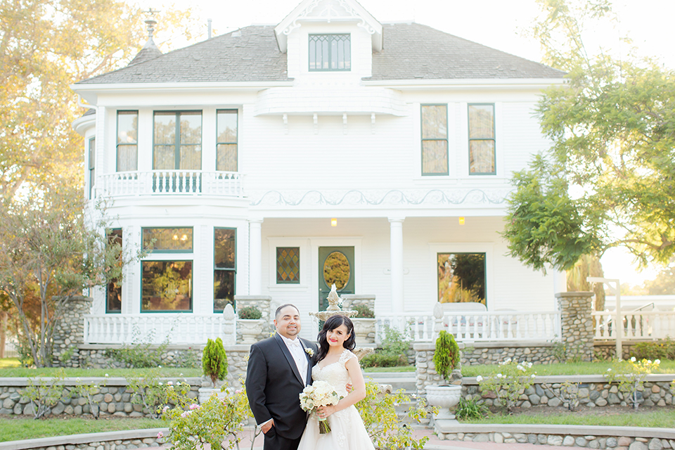 Orange county outdoor summer wedding at the heritage museum bride ball gown with lace straps and a sweetheart neckline with a short tulle skirt and long veil with groom black shawl lapel tuxedo with a white dress shirt and white vest with a white tie and white floral boutonniere hugging and bride holding white floral bridal bouquet