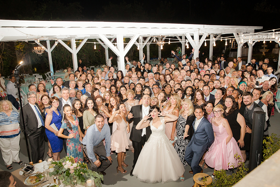 Orange county outdoor summer wedding at the heritage museum bride ball gown with lace straps and a sweetheart neckline with a short tulle skirt and long veil with groom black shawl lapel tuxedo with a white dress shirt and white vest with a white tie and white floral boutonniere standing with wedding guests at end of night