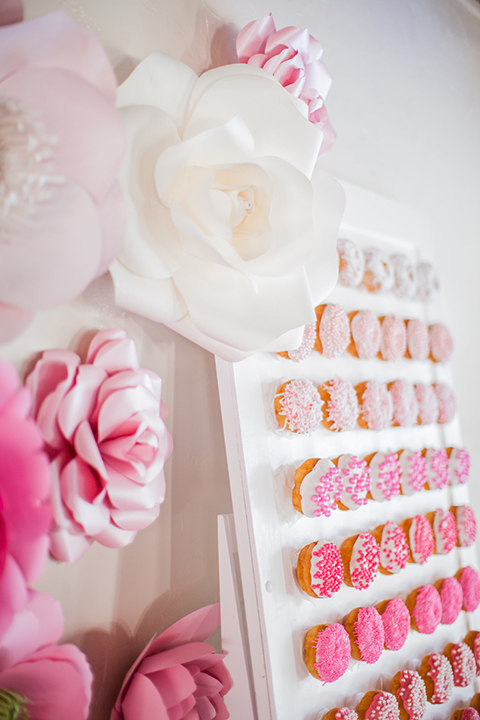 San clemente beach wedding shoot at ole hanson beach club table set up with white table floral linen and blush pink flower centerpiece decor with white and gold place settings with pink menus and glassware with a pink ombre donut wall and paper flowers