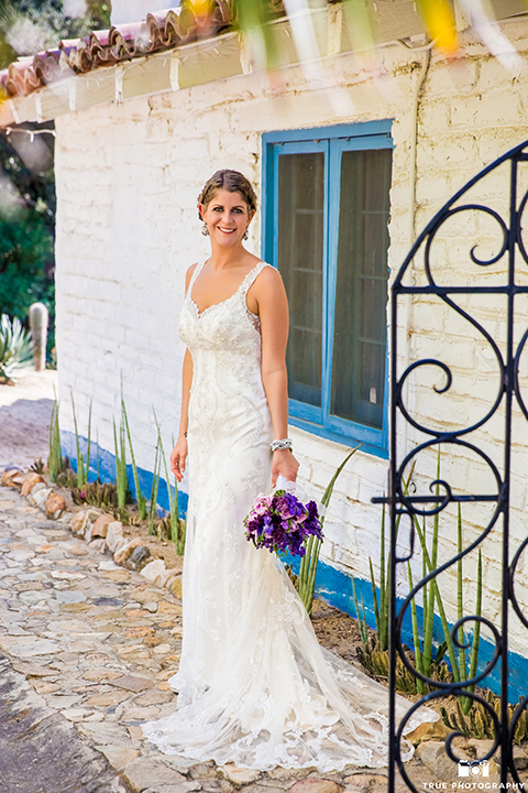 San diego outdoor wedding at leo carillo ranch bride form fitting gown with a sweetheart neckline with thin straps and beaded detail on bodice holding purple floral bridal bouquet 