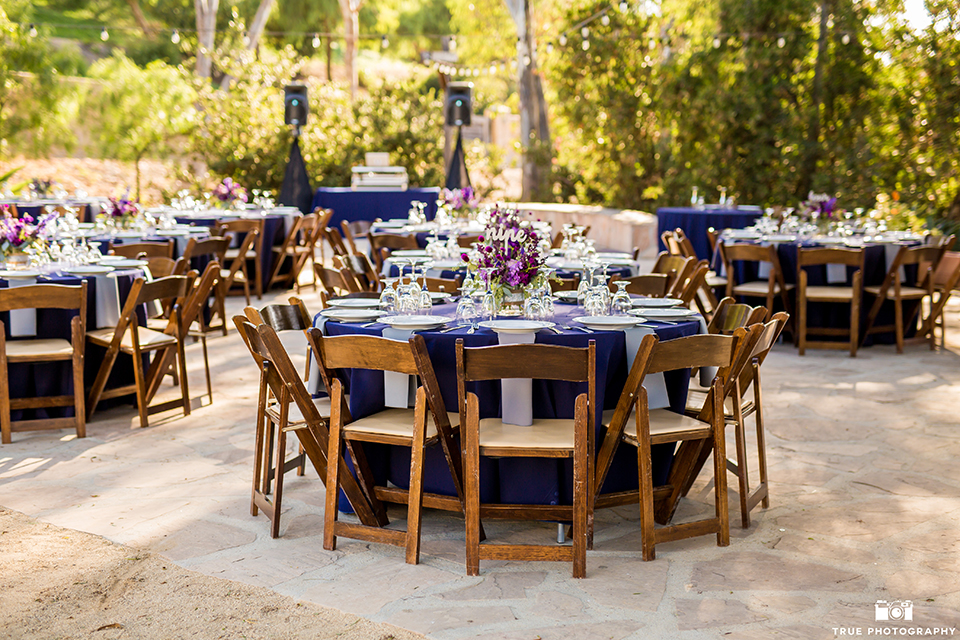 San diego outdoor wedding at leo carillo ranch reception table set up with purple linen and brown chairs with white place settings and light purple napkin decor with purple flower centerpiece decor 