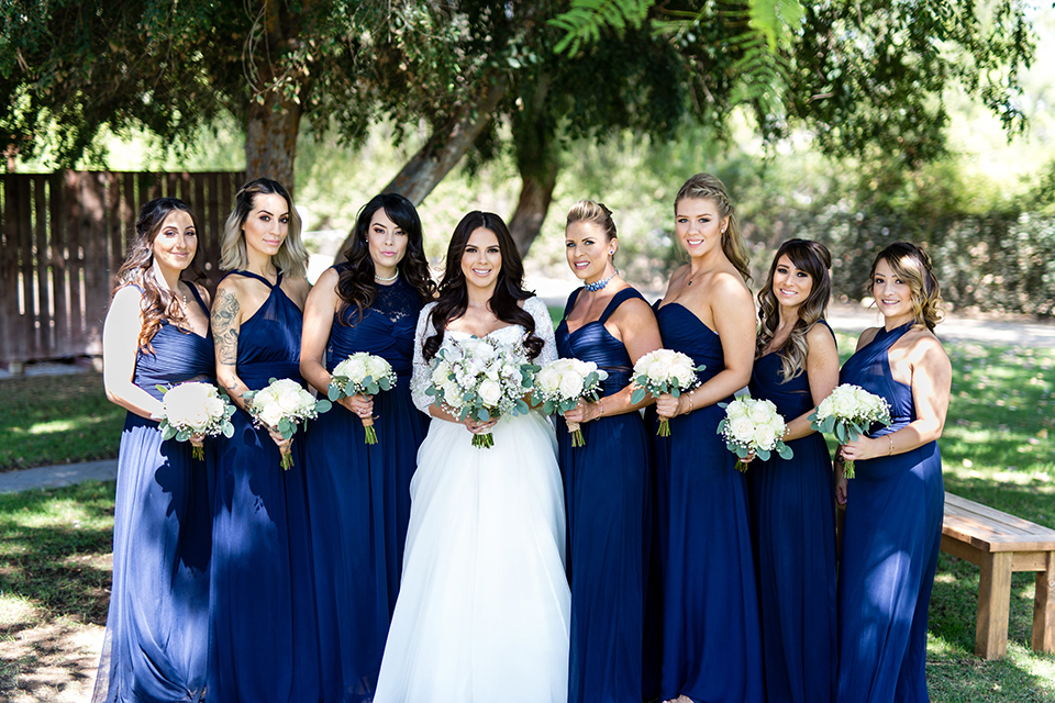 Temecula outdoor wedding at bella gardens estates bride lace ball gown with long sleeves and a sweetheart neckline with a tulle skirt holding white and green floral bridal bouquet with bridesmaids long navy dresses with white floral bridal bouquets