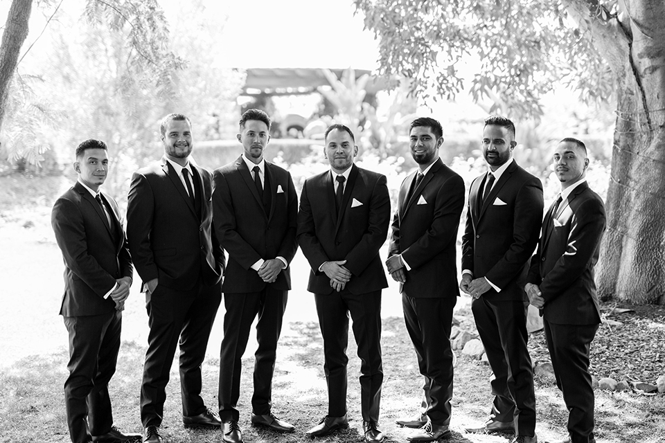 Temecula outdoor wedding at bella gardens estates groom navy shawl lapel tuxedo with a matching vest and white dress shirt with a long navy blue tie and white floral boutonniere with groomsmen navy tuxedos with long navy blue ties