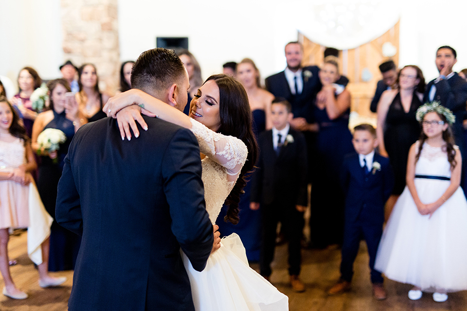 Temecula outdoor wedding at bella gardens estates bride lace ball gown with long sleeves and a sweetheart neckline with a tulle skirt and groom navy shawl lapel tuxedo with a matching vest and long navy blue tie with a white floral boutonniere first dance at reception