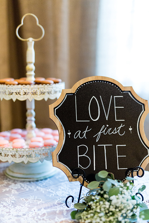 Temecula outdoor wedding at bella gardens estates wedding reception dessert table white linen with assortment of desserts with black and white sign and three tier white wedding cake with white flowers on top and pearl design 