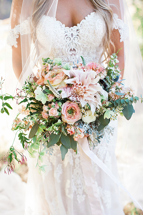 California outdoor wedding at the rancho san antonio bride form fitting lace gown with off the shoulder straps and a sweetheart neckline with a flower crown holding white and green floral bridal bouquet close up